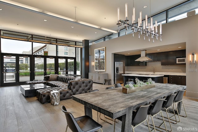 dining space featuring a high ceiling, a chandelier, french doors, and light hardwood / wood-style flooring