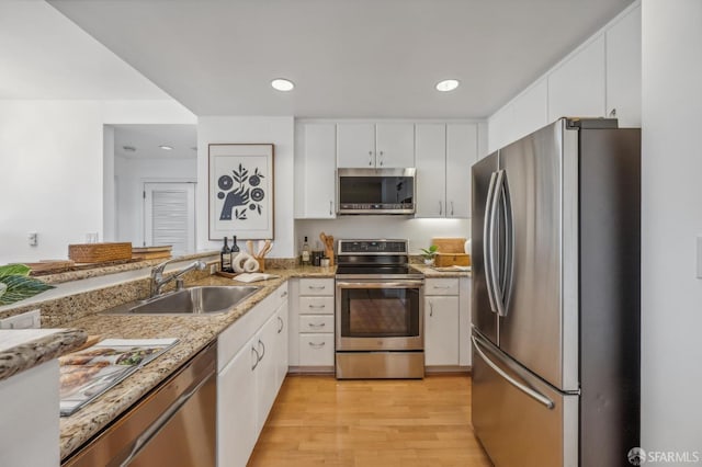 kitchen featuring stainless steel appliances, light stone counters, white cabinets, sink, and light hardwood / wood-style flooring