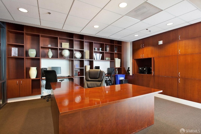 office space featuring dark colored carpet, built in shelves, and a paneled ceiling