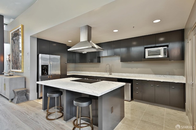 kitchen with stainless steel appliances, light stone counters, a kitchen bar, range hood, and a center island