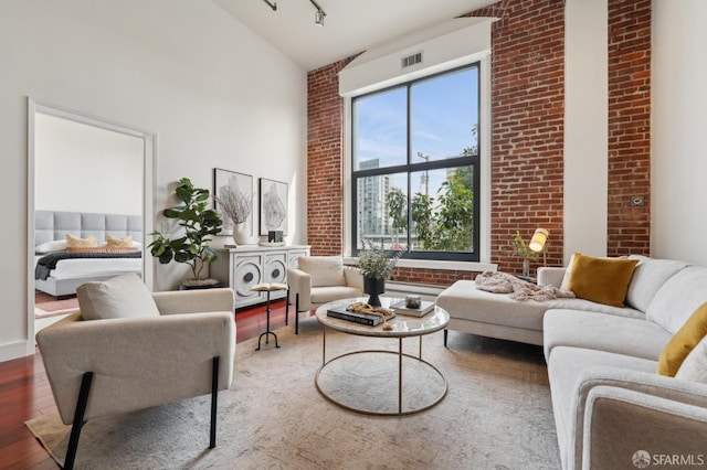 living room featuring high vaulted ceiling, visible vents, brick wall, and wood finished floors