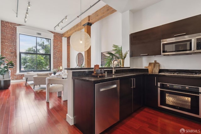 kitchen featuring brick wall, dark wood-type flooring, a sink, appliances with stainless steel finishes, and dark stone countertops