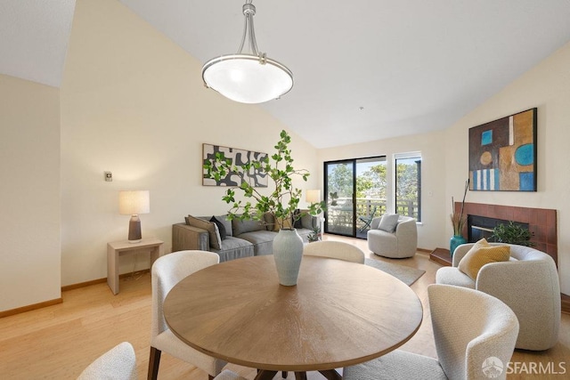 dining room with high vaulted ceiling, a glass covered fireplace, light wood finished floors, and baseboards