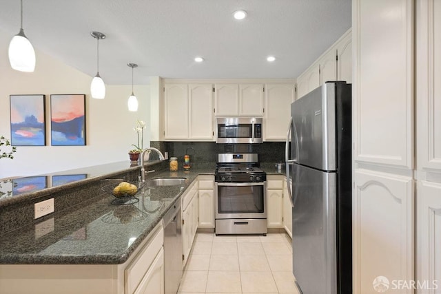 kitchen with dark stone countertops, a sink, light tile patterned floors, a peninsula, and appliances with stainless steel finishes