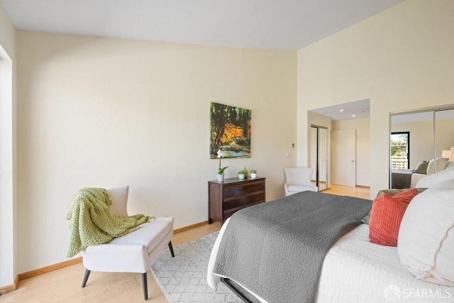 bedroom featuring lofted ceiling, baseboards, multiple closets, and wood finished floors