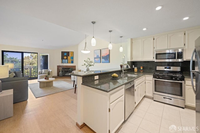 kitchen with a peninsula, a sink, dark stone countertops, open floor plan, and appliances with stainless steel finishes