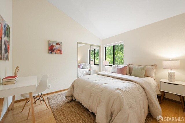 bedroom featuring light wood finished floors, baseboards, and high vaulted ceiling