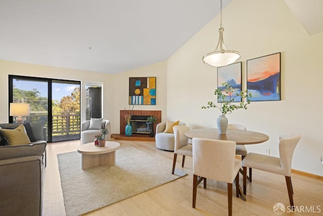 interior space with vaulted ceiling, a brick fireplace, and light wood finished floors