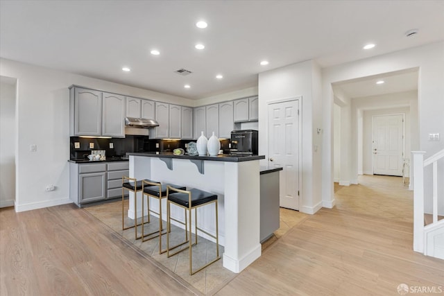 kitchen with a center island, a kitchen bar, light hardwood / wood-style floors, backsplash, and gray cabinets