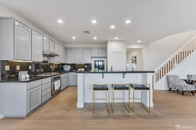 kitchen featuring a breakfast bar, an island with sink, gray cabinets, and stainless steel appliances