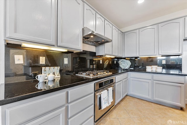 kitchen featuring stainless steel appliances, light tile patterned flooring, tasteful backsplash, and dark stone counters