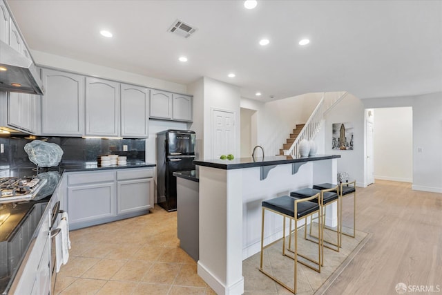 kitchen with black fridge, a breakfast bar area, stainless steel gas stovetop, backsplash, and range hood