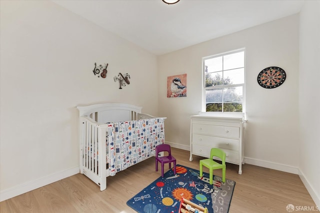 bedroom with a nursery area and light wood-type flooring