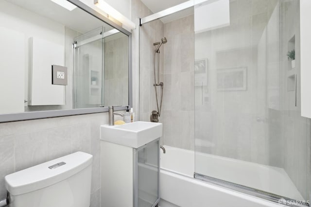 full bathroom featuring toilet, vanity, enclosed tub / shower combo, and tile walls