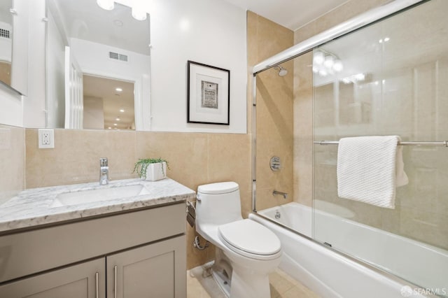 full bathroom with tile patterned floors, bath / shower combo with glass door, toilet, vanity, and tile walls