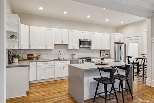 kitchen with sink, a kitchen island, a kitchen breakfast bar, white cabinets, and appliances with stainless steel finishes