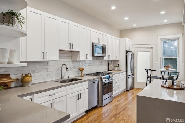 kitchen featuring decorative backsplash, light wood-type flooring, stainless steel appliances, sink, and white cabinetry