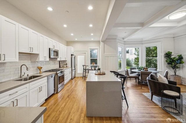 kitchen with white cabinetry, sink, a center island, light hardwood / wood-style floors, and appliances with stainless steel finishes