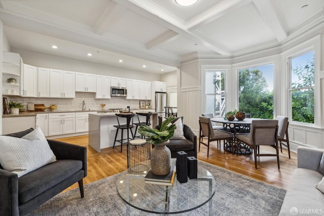 living room with coffered ceiling, crown molding, beamed ceiling, and light hardwood / wood-style flooring