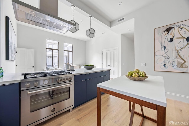 kitchen with blue cabinetry, wall chimney range hood, high end range, and light hardwood / wood-style floors