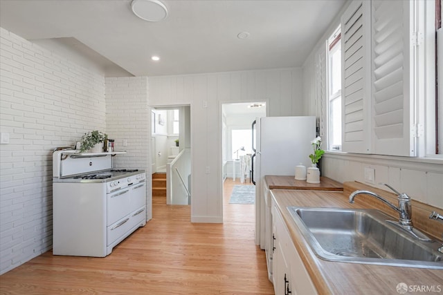 kitchen with brick wall, white appliances, a sink, white cabinets, and light wood-style floors