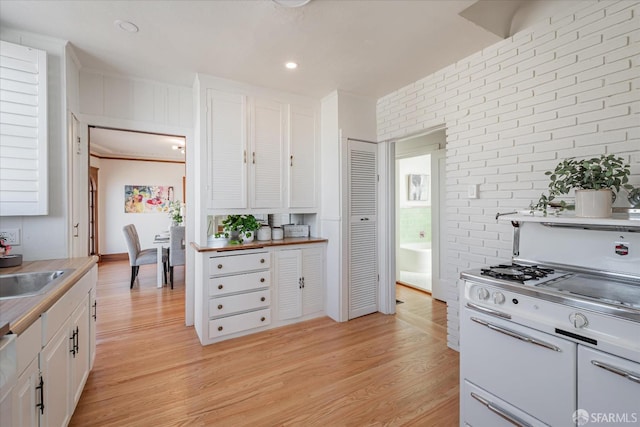 kitchen with light wood finished floors, white range with gas cooktop, white cabinets, brick wall, and light countertops