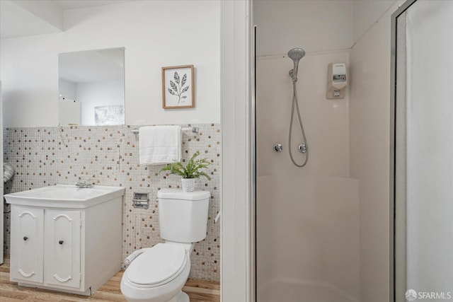 bathroom featuring a stall shower, toilet, wood finished floors, vanity, and tile walls