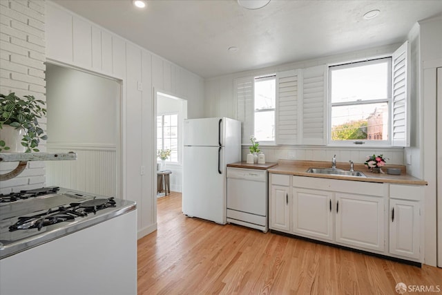 kitchen with white appliances, light countertops, light wood-type flooring, white cabinetry, and a sink