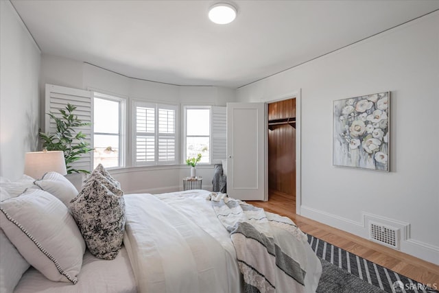 bedroom with light wood-style flooring, visible vents, a walk in closet, and baseboards