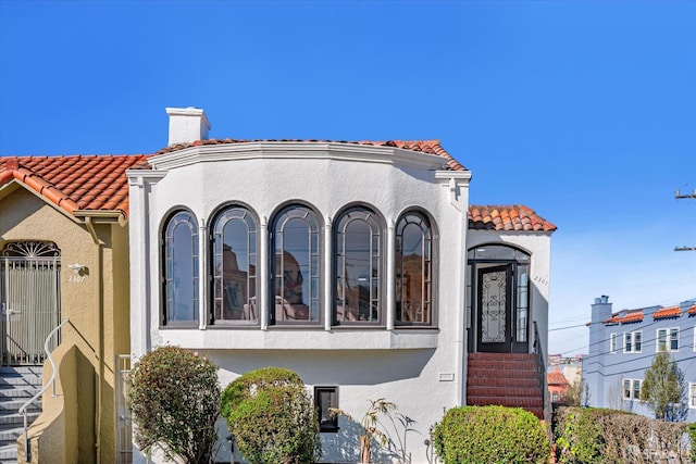 view of front of property featuring a chimney, a tiled roof, and stucco siding