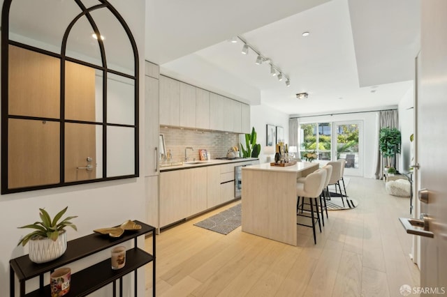 kitchen featuring a center island, tasteful backsplash, light wood-type flooring, sink, and a breakfast bar area