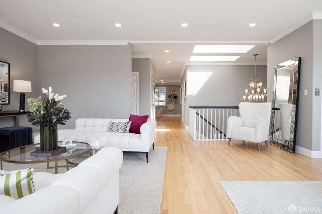 living room featuring a skylight, light wood-type flooring, crown molding, and an inviting chandelier