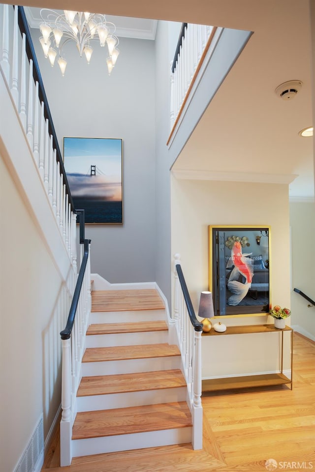 staircase with a notable chandelier, crown molding, and hardwood / wood-style flooring