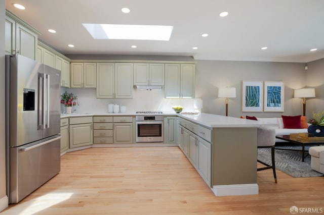 kitchen featuring kitchen peninsula, light hardwood / wood-style floors, stainless steel appliances, and a breakfast bar