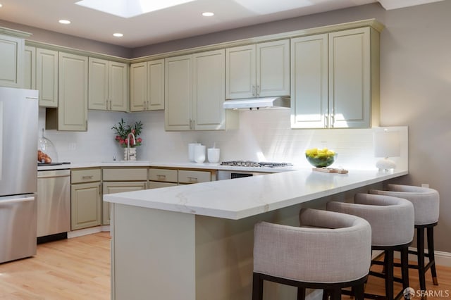 kitchen featuring kitchen peninsula, a kitchen bar, stainless steel appliances, and light wood-type flooring