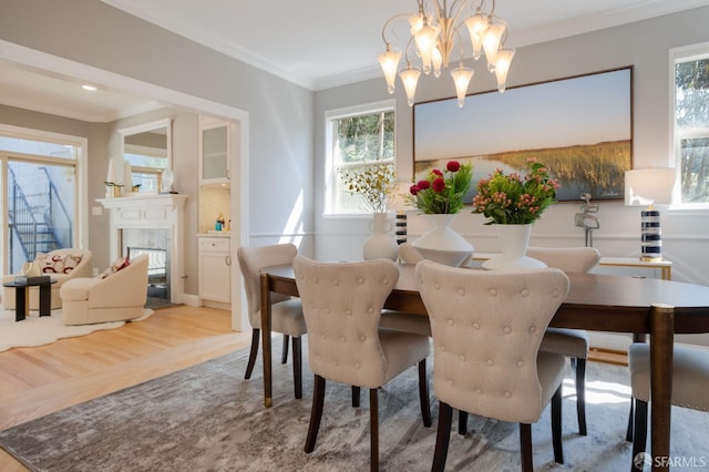 dining area with crown molding, a wealth of natural light, a high end fireplace, and light hardwood / wood-style flooring