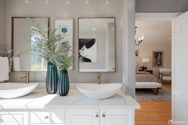 bathroom featuring wood-type flooring, vanity, ornamental molding, and an inviting chandelier