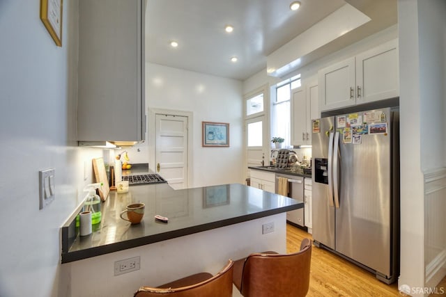 kitchen featuring sink, white cabinets, kitchen peninsula, light hardwood / wood-style flooring, and appliances with stainless steel finishes