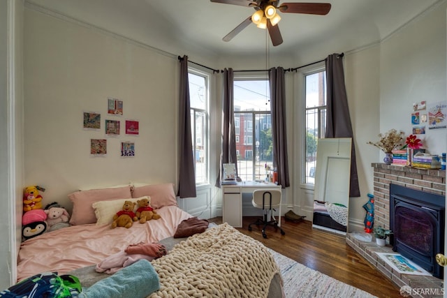 bedroom with multiple windows, dark hardwood / wood-style floors, ceiling fan, and a brick fireplace