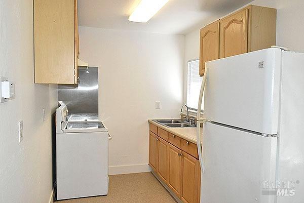 kitchen with baseboards, light countertops, freestanding refrigerator, washer / clothes dryer, and a sink