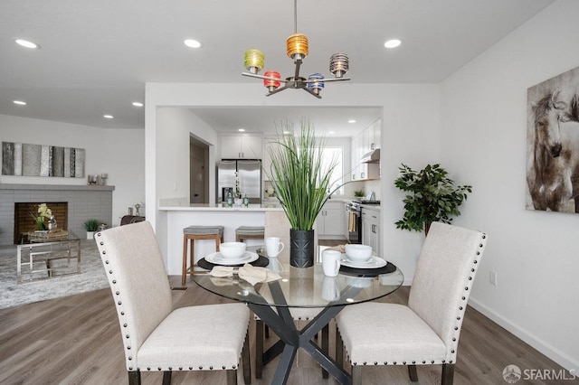 dining area with hardwood / wood-style floors, a chandelier, and a brick fireplace