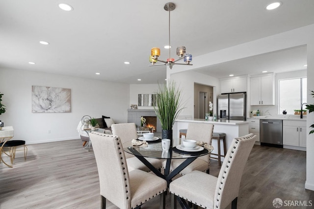 dining space with a brick fireplace, a chandelier, and light hardwood / wood-style flooring