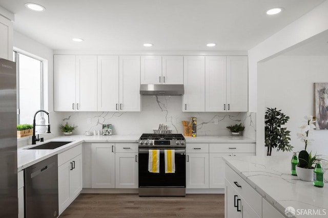 kitchen with hardwood / wood-style floors, appliances with stainless steel finishes, sink, light stone counters, and white cabinetry