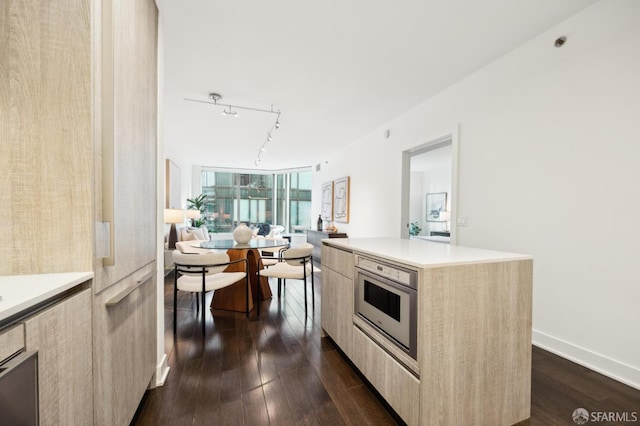 kitchen with oven, a kitchen island, light brown cabinets, track lighting, and dark hardwood / wood-style flooring