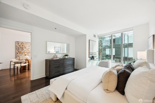 bedroom with a wall of windows and dark hardwood / wood-style floors