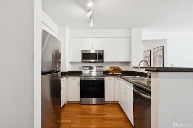 kitchen featuring a sink, dark countertops, wood finished floors, stainless steel appliances, and white cabinets