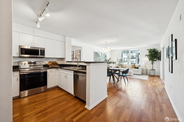 kitchen with a sink, dark countertops, dark wood-style floors, open floor plan, and appliances with stainless steel finishes