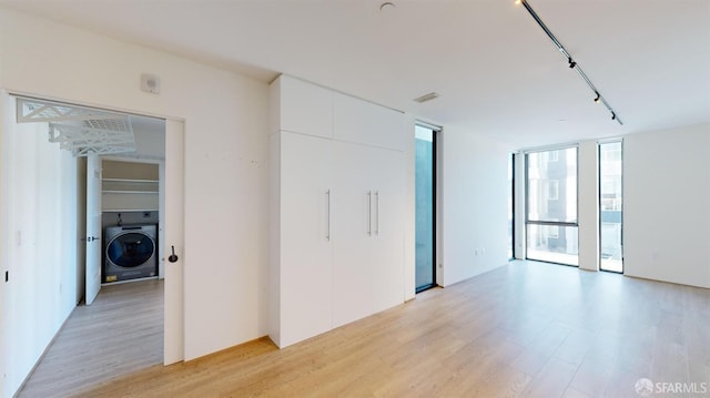 spare room with rail lighting, light hardwood / wood-style flooring, expansive windows, and washer / dryer