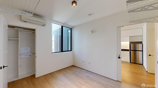 unfurnished bedroom featuring stainless steel fridge, a closet, a wall mounted air conditioner, and light wood-type flooring