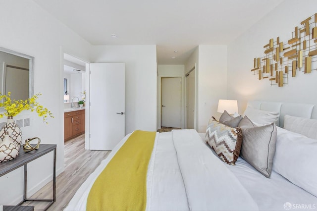 bedroom with ensuite bath, light hardwood / wood-style floors, sink, and a closet